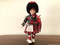 Front view of the vintage Scottish piper doll showing full traditional tartan outfit, black fur hat with red pom, bagpipes, and white sporran.