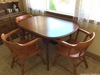 Expandable oval dining table with turned legs and two leaves with three of six matching chairs.