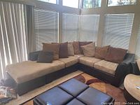 Full view of the 3 piece sectional couch in a sunroom corner, showcasing the leather frame and beige suede cushions with assorted pillows.