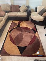 Photo of the area rug laid on the floor next to sofas and chairs; shows the pattern and colors.