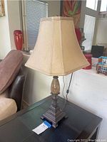Full view of ceramic table lamp with beige fabric shade, stone accent, and ornate base on black table near sofa.