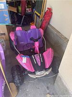 Front view of pink and purple Children's Dune Racer electric ride-on car with large rugged tires in a garage setting.