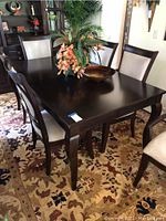 Front top angle of dark wood rectangular dining table with cabriolet legs, on floral carpet, with decorative centerpiece.