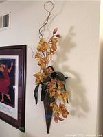 First floral sconce angled slightly left, showing orange orchid flowers with realistic petals, green leaves, and twisted wire extensions in a woven basket holder.