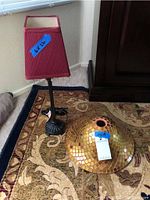 Small lamp with red lampshade next to a mosaic glass lampshade on a carpeted floor.