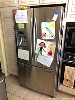 Closed view of Samsung refrigerator with French doors and bottom freezer drawer, stainless steel, with children's drawings and notes attached to the front.