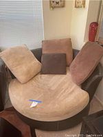 Swivel chair angled front showing seat cushion and pillows on leather frame next to window.