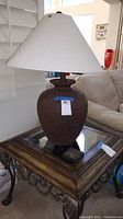 Full view of ceramic table lamp sitting on an ornate glass and metal side table next to a couch.