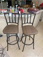Front view of two brown upholstered bar stools with black metal bases and backrests placed in a kitchen area.
