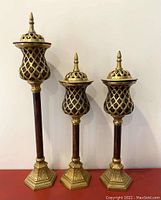 Three decorative candle holders of varying heights with removable lattice-style lids placed on top, showing intact condition and detailed metalwork.