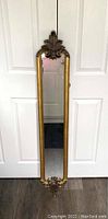 Front view of the narrow, tall mirror showing gold frame with decorative carved top and bottom.