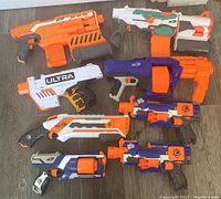 Top down photo showing all eight Nerf blasters arranged on the floor, displaying a variety of styles and colors.
