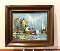 Framed oil on board painting showing the entire framed artwork, featuring boats, lighthouse, and rustic building in a harbor scene.