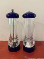 Two tall pepper mill and salt shaker units with cobalt blue tops and bases, clear lucite bodies. Pepper mill has metal grinding knob on top.