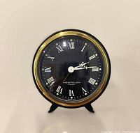Front view of vintage Westclox alarm clock showing black face with white Roman numeral hour markers, gold bezel, and clock hands.
