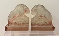 Front view of two glass ram bookends showing detailed texture and pinkish color