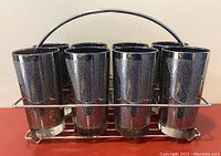 Eight vintage mid-century highball glasses with silver textured overlay arranged in metal wire caddy, visible front view.