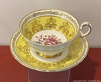 Photo of vintage Paragon teacup and saucer on display, showing gold and yellow detailing with floral center.