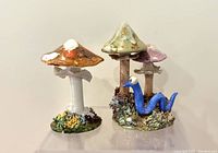 Photo showing two vintage Richard Ogner pottery mushrooms, one orange-brown mushroom on green base, and one two-mushroom piece with blue slug figure.