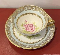 Teacup and saucer displayed together showing pink rose and gold design on white porcelain.
