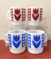 Four vintage Termocrisa milk glass mugs shown with two featuring blue tulip and checkered design in front and two with red design behind.