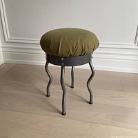 Front angle view of the 1995 IKEA Uri stool showing green cushioned top and grey metal legs on a wood floor.
