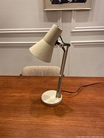 Cream-colored adjustable Mid-Century Modern desk lamp by Lyskaer positioned on a wooden table against a paneled wall.