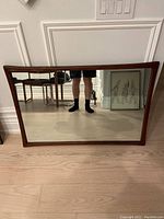 Full front view of rectangular walnut-framed mirror leaning against wall