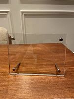 Front view of the clear acrylic photo frame with metal rods on a wooden table against a white paneled wall.