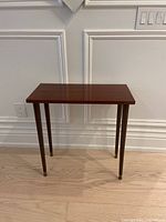 Full view of the mid-century modern laminated rosewood console table showing rectangular top and four tapered legs with brass caps.