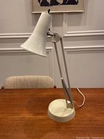 Full view of the vintage Mid-Century Modern Luxo task lamp on wooden table, showing the adjustable arm and bell-shaped shade.