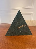 Front and angled view of the triangular green marble clock showing gold-tone clock hands and smooth polished surface.