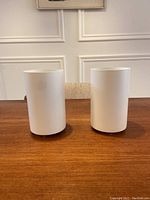 Pair of white cylindrical mid century canister lamps on wood table, front view, unlit.