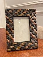 Front and angled view of the multicolored marble mosaic photo frame on a wooden table against white paneled wall.