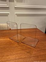 Pair of clear acrylic L-shaped bookends placed on a wooden surface.