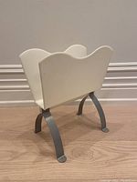 Front angle view of the Per-Ivar Ledang magazine holder showing the white plastic container and curved metal legs.