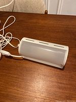 White vintage Ikea wall lamp viewed from front resting on wood surface, showing curved rectangular shape and cord with switch.