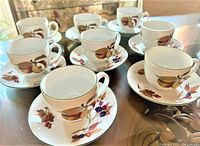 Set of 8 cups and saucers on a glass table, showing variety of fruit decoration