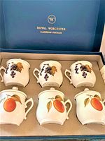Set of six Royal Worcester porcelain chocolate cups with two fruit designs (grapes and peaches), all with lids, set shown in original box with Royal Worcester branding on lid interior.