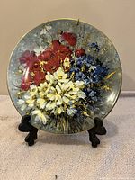 Top front view of the Royal Doulton collectors plate displaying colorful floral bouquet detail on plate face, positioned on a black stand against a neutral fabric background.