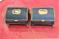 Closed view of the two decorative boxes showing ornate gold plaques on dark textured exterior with clasp and claw feet.