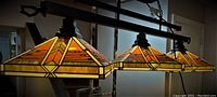 Frontal view of the three stained glass pendant lamp shades mounted on a horizontal dark metal fixture.
