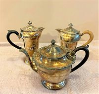 Three vintage silver-plated tea and coffee pots grouped together on a cloth surface with focus on their shapes and handles.