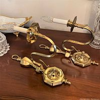 Two vintage polished brass wall sconces on a wooden surface showing details of the arm and wall mount.