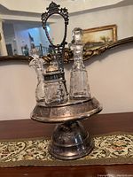 Full view of antique silver plate castor condiment set with etched glass bottles and ornate handle.