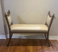Front view of the wooden bench showing champagne fabric seat and backrest, dark wood frame, curved legs, and tassels.