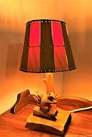 Front angle of the lamp showing wood base with squirrel carving and striped lampshade lit up