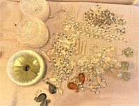 Wide view of chandelier parts including frosted glass ceiling light covers and assorted crystal drops, prisms and chains scattered on a beige textured fabric surface.