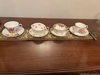 Top view of four cups and saucers aligned on a tablecloth showing floral patterns and gold trim