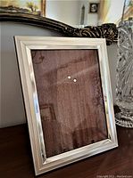 Front view of the polished rectangular silver photo frame with wooden backing reflecting ambient light